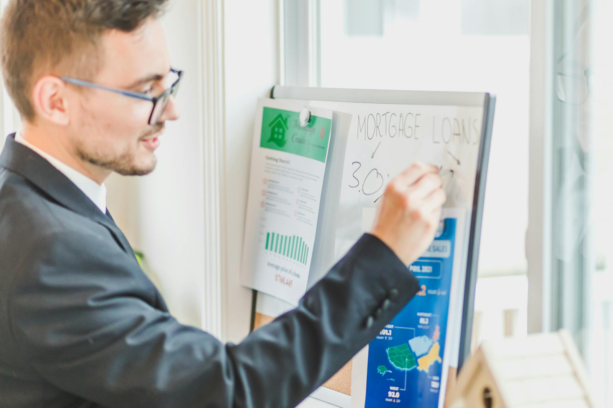 Businessman in suit writes on whiteboard displaying mortgage loan rates during a real estate meeting.